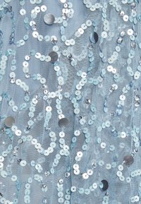 Ljusblått nätfabric med spridda runda paljetter i varierande storlekar, vilket skapar ett texturerat mönster med glänsande och matta ytor.