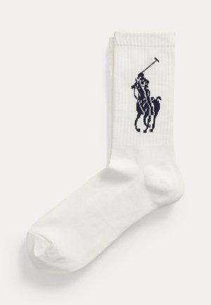 Hvid ribstrikket ankelsok med et sort logo af en polo-spiller til hest broderet nær toppen.