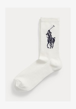 Witte geribbelde sneakersok met een zwart paardenrijder-polo-logo geborduurd vlakbij de bovenkant.