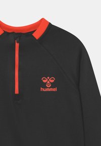 Svart fleece-pullover med halvdragkedja, med en ljusröd krage och dragkedjedetalj. Hummel-logotyp i rött på bröstet. Texturerad tyg.