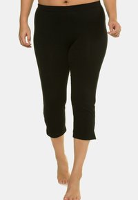 Leggings capri neri realizzati in tessuto elasticizzato, con vita media e design aderente, che terminano sotto il ginocchio con orlo pulito.