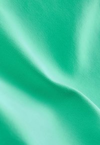 Zbliżenie gładkiej, turkusowej tkaniny z widoczną drobną fakturą oraz miękkimi zagięciami tworzącymi delikatne cienie i refleksy świetlne.