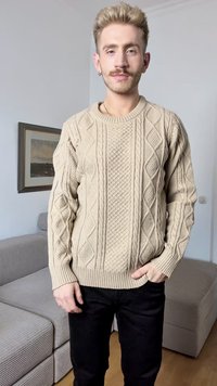 Suéter tricotado em creme com padrões texturizados de ponto de cabos, decote redondo e punhos canelados, usado com calças pretas. Tecido macio e espesso.