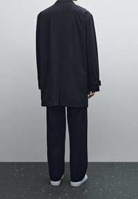 Marineblauer oversized Blazer mit einem Sch vent, kombiniert mit locker sitzenden marineblauen Hosen und weißen Sneakers auf einem strukturierten schwarzen Boden.