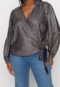 Blusa blu navy con motivo dorato, design avvolgente e dettaglio con fiocco in vita. Presenta maniche lunghe e colletto. Tessuto morbido e liscio.