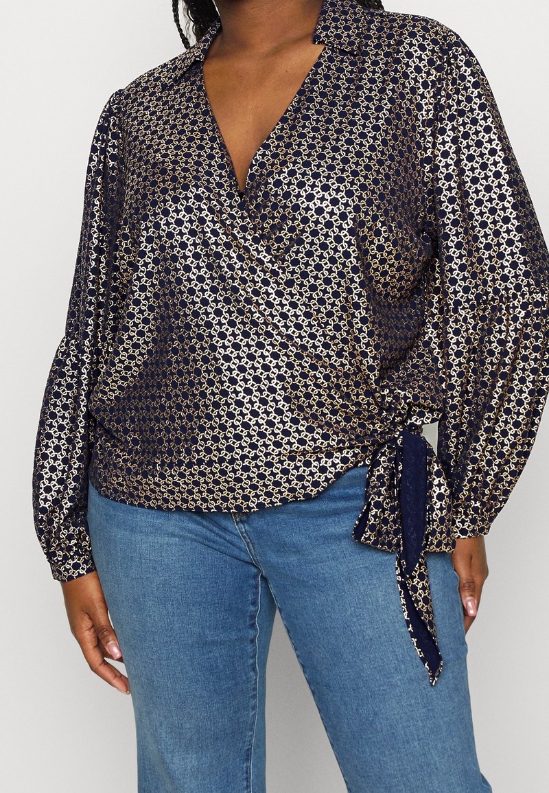 Blusa blu navy con motivo dorato, design avvolgente e dettaglio con fiocco in vita. Presenta maniche lunghe e colletto. Tessuto morbido e liscio.