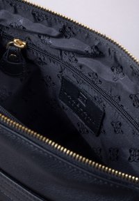 Black leather bag interior with a gold zipper. Lined with black fabric featuring a subtle pattern. Includes a leather label inside.
