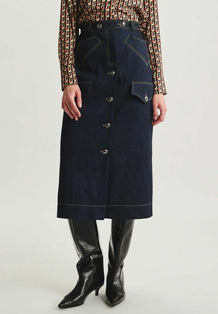 Jupe en denim bleu foncé avec une coupe mi-longue, des boutons sur le devant et deux grandes poches. Les coutures contrastées mettent en valeur le design.