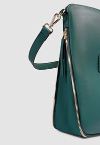 Teal eco-lederen tas met een gestructureerde vorm, gouden hardware en een contrasterende ritsafwerking. Voorzien van een afneembare schouderband voor veelzijdigheid.