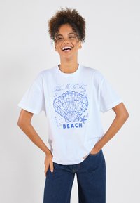 Vit bomull t-shirt med en blå snäcka grafisk design och texten "Ta mig till STRANDEN" under den, korta ärmar och avslappnad passform.