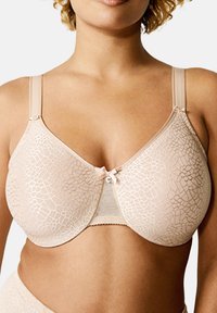 Beige bra with a floral lace pattern, semi-sheer cups, adjustable straps, and a small bow accent at the center front.