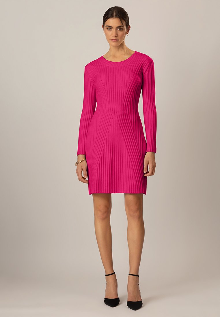 Rosa geripptes Kleid mit langen Ärmeln, leichtem Stoff, figurbetontem Schnitt und vertikalen Linien. Getragen mit schwarzen spitzen Absatzschuhen und minimalem Schmuck.