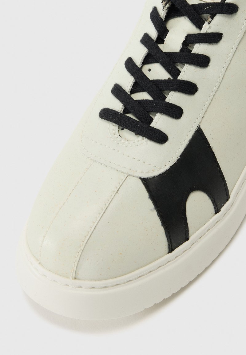 Witte leren sneaker met een zwarte accent, gestructureerd oppervlak, ronde neus en zwarte veters. Dikke zool met een gladde afwerking.