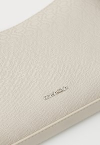 Borsa Calvin Klein in materiale sintetico crema con un motivo in rilievo di forme interlocking, con dettaglio del logo argento su un lato.