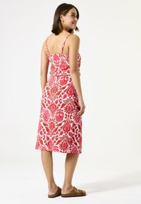 Kleurige midi-jurk met spaghettibandjes, met een rood en roze bloemmotief op een witte achtergrond. Draag met bruine sleehakken.