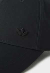 Black baseball cap with a textured fabric, curved brim, and a matte black Adidas logo on the front. Detailed stitching visible.