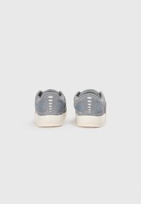 Sneaker in suede grigio con una superficie liscia, dettagli blu chiaro e suola in gomma crema. Presenta un collare imbottito e perforazioni circolari.