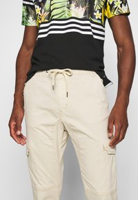 T-shirt noire à manches courtes avec imprimé floral et rayures blanches, associée à un short cargo beige clair avec cordon de serrage et poches latérales.