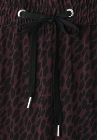 Close-up of dark purple fabric with black irregular spots and black drawstring tied in a bow through silver eyelets at elastic waistband.
