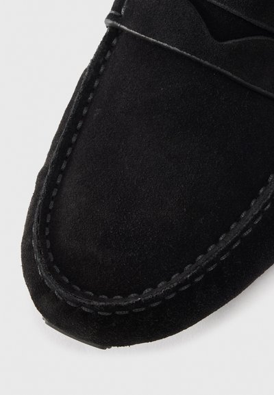 Black suede moccasin with a rounded toe, featuring contrast stitching and a decorative leather band across the upper.