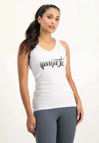 Weißes Tanktop mit "Namaste" in schwarzer Schreibschrift, enganliegendes Design, weicher Stoff und breite Träger, kombiniert mit grauen Leggings.