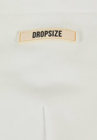 White fabric with a stitched seam features a prominent beige label reading "DROPSIZE" in black uppercase letters.
