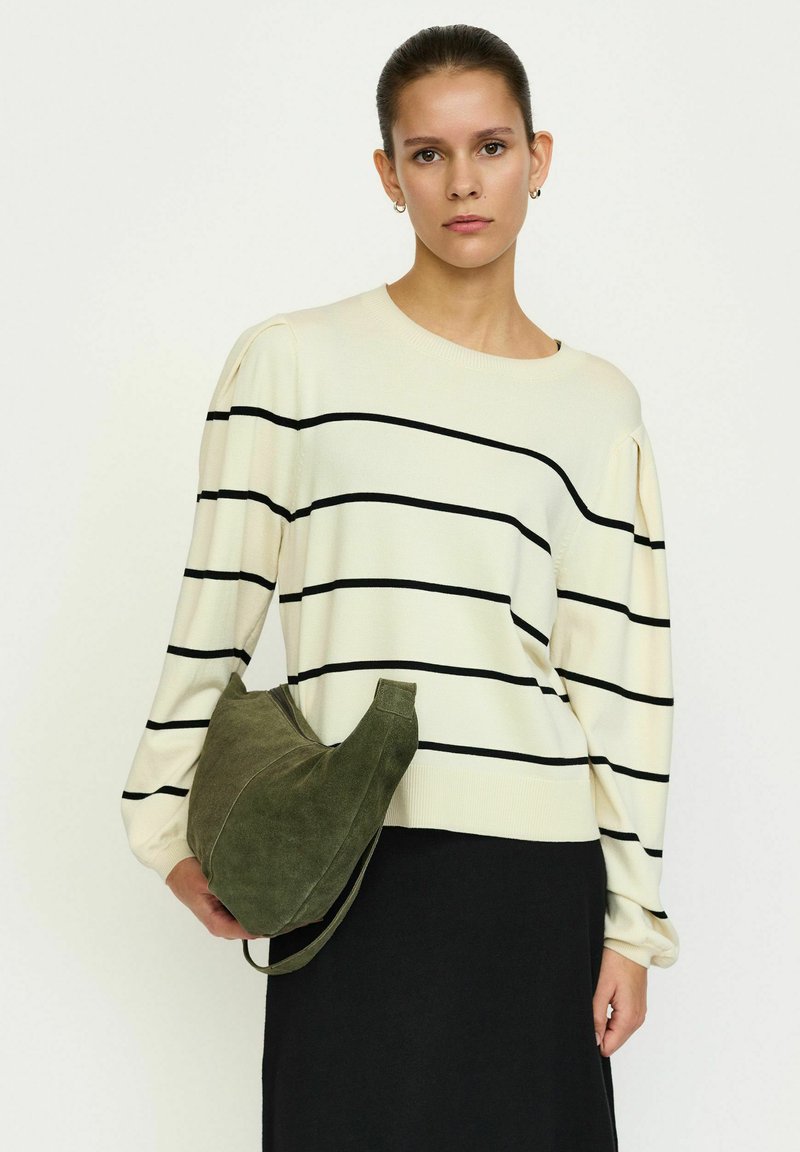 Maglione crema con strisce orizzontali nere, presenta maniche lunghe a sbuffo. Tieni una borsa in suede verde scuro. Gonna nera visibile.