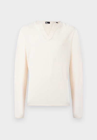 Κρεμ πουλόβερ με V-λαιμόκοψη και μακριά μανίκια, με μικρό γιακά και ετικέτα στο εσωτερικό του λαιμού, σε απλό φόντο.