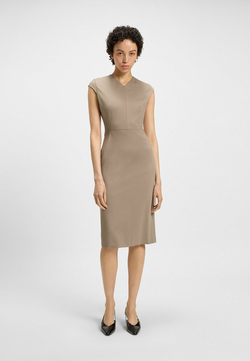 Beige fitted dress with cap sleeves, V-neckline, and seam detailing. The smooth fabric extends to knee length, paired with black heels.