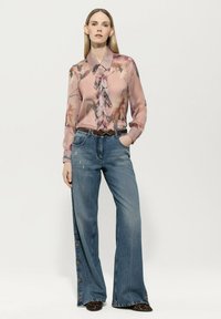 Long-sleeve pink blouse with floral pattern and ruffles at front, paired with wide-leg blue denim jeans featuring side button detail.