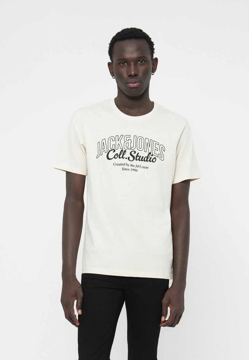 T-shirt en coton crème avec lettrage noir "JACK & JONES Coll. Studio", col rond et manches courtes.
