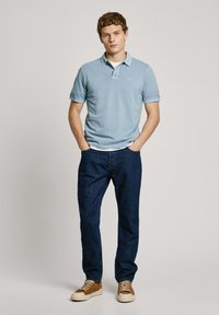 Light blue polo shirt with short sleeves, paired with dark blue jeans and brown sneakers. Simple design, no visible patterns or logos.