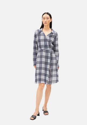 Blau-weißes Karohemdkleid aus leichter Stoffqualität. Verfügt über einen Kragen, eine durchgehende Knopfleiste, einen Taillengürtel und lange Ärmel. Schwarze Absatzsandalen.