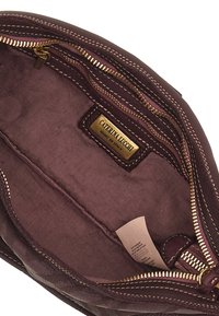 Interno di una borsa in pelle bordeaux scuro con cerniera dorata. Fodera in tessuto che presenta una sottile trama. L'etichetta riporta "Caterina Lucchi, Made in Italy."