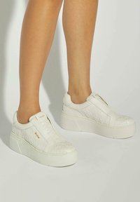 White slip-on sneakers with a textured quilted design, platform sole, smooth leather material, and subtle gold logo accent.