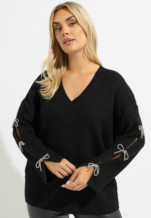 Maglione nero lavorato a maglia con scollo a V e maniche lunghe, caratterizzato da accenti di nastro argento nei dettagli ritagliati sui gomiti. Design testurizzato.