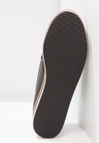 Chaussure noire avec une semelle en caoutchouc texturée, présentant des rainures horizontales. Le côté est orné d'une bordure contrastante de couleur claire.