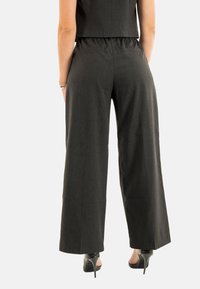 Pantaloni neri a gamba larga con un motivo a strisce texturizzato, cintura elastica e un design fluido. Abbinati a scarpe con tacco nere.