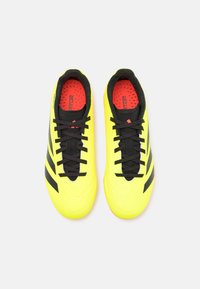 Scarpe da calcio giallo brillante con strisce nere, superficie testurizzata, lacci neri e soletta rossa. Design leggero per le prestazioni.