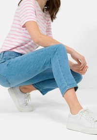 Jeans de mezclilla azul claro con un dobladillo recortado, combinados con una camiseta blanca de rayas con rayas rosas y zapatillas blancas.