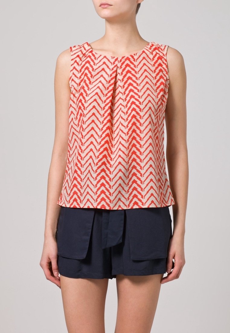 Top senza maniche di color crema con un motivo a zigzag rosso, caratterizzato da un frontale plissettato e una vestibilità ampia. Abbinato a pantaloni corti blu navy. Tessuto testurizzato.
