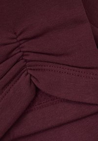Bordeaux strikket stoff som viser rynket tekstur med synlige sømmer, og gir et mykt, jevnt utseende og fleksibel design.