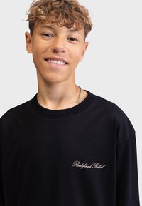 Svart bomulls t-skjorte med rund hals og korte ermer, med "Redefined Rebel" brodert i beige på venstre bryst.