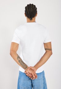 Hvid kortærmet tætsiddende t-shirt lavet af ribbet stof. Har en rund halsudskæring og en glat tekstur, parret med blå denim shorts.