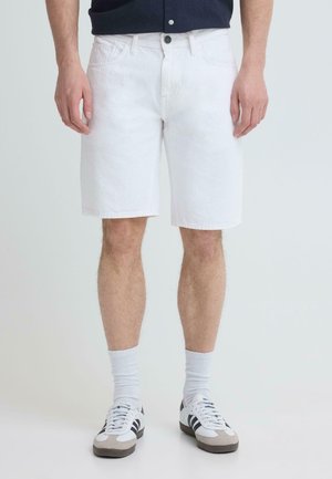 Mannelijke model draagt witte knielange short, witte sokken en witte sneakers met zwarte strepen, staand tegen een effen lichte achtergrond.