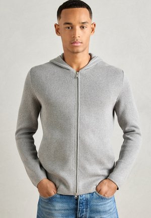 Light gray zip-up hoodie with a textured knit pattern, featuring a hood and long sleeves, paired with blue denim jeans.