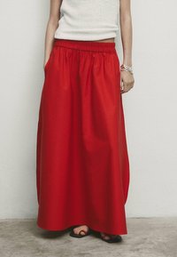 Jupe maxi rouge avec une taille élastique, en tissu lisse. Dotée de poches latérales et d'un design fluide. Couleur unie, simple.