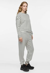 Ensemble de vêtements de détente rayés en crème et noir, comprenant un haut à manches longues décontracté et un pantalon assorti avec des poignets et une taille élastiques. Baskets noires.