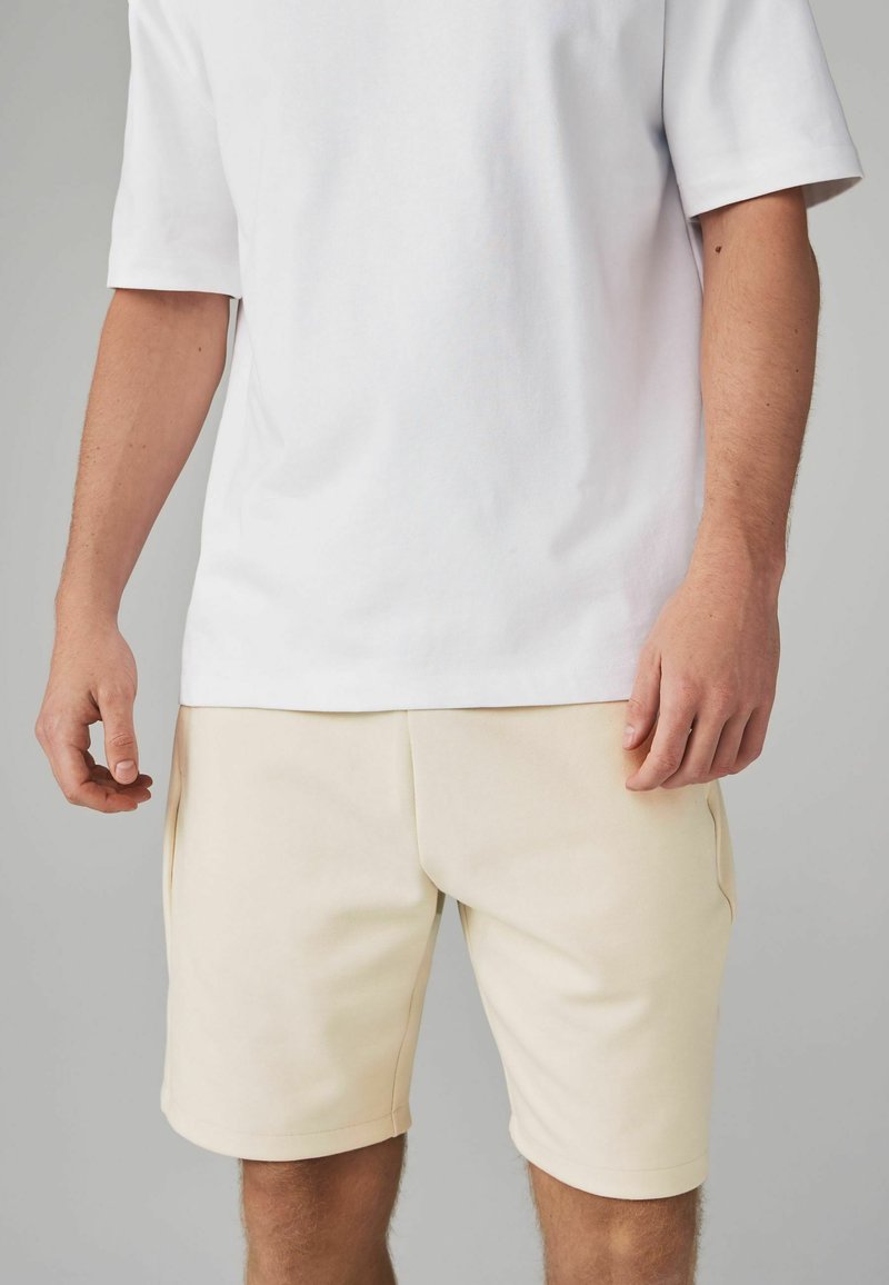 Witte T-shirt met korte mouwen in combinatie met crèmekleurige shorts. De shorts hebben zijzakken en een gladde stofstructuur. Eenvoudig, strak ontwerp.