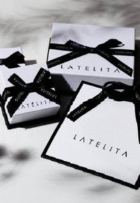 White gift boxes with black satin ribbons, featuring "LATELITA" in bold black lettering. Smooth texture with a sleek, modern design.